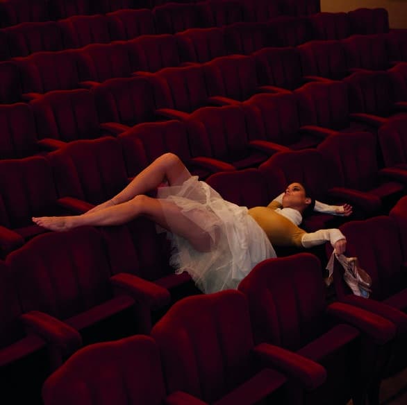 Figura distesa tra le poltrone rosse di un teatro
