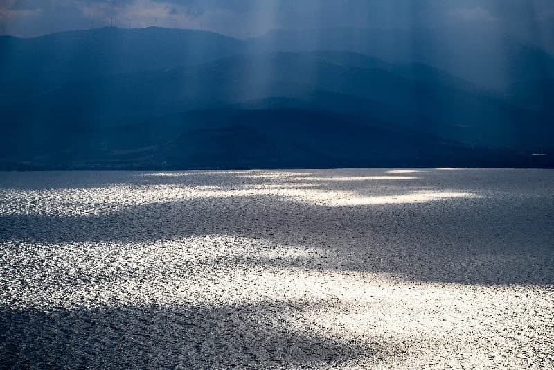 Energy di Angelo Golizia: fasci di luce e riflessi sul mare davanti ai rilievi di Nafplio.